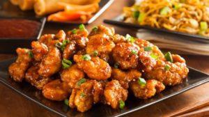 Crispy orange chicken garnished with green onions, served on a black plate