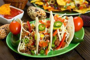 Filled tacos topped with fresh tomatoes, onions, and jalapeños on a green plate